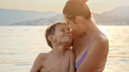 Téléchargez les photos : Jeune mère sur la plage de la mer embrassant et embrassant son fils. Vacances, vacances d'été et tourisme. - en image libre de droit