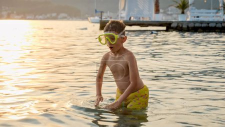 Téléchargez les photos : Joyeux garçon joyeux en masque de plongée en apnée plongeant dans l'eau de mer sur la plage et souriant à la caméra. Vacances, vacances d'été et tourisme. - en image libre de droit