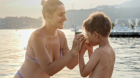 Foto de Sonriente madre poniéndose una máscara de snorkel en su pequeño hijo antes de que él nadara en el mar. Vacaciones, vacaciones de verano y turismo. - Imagen libre de derechos
