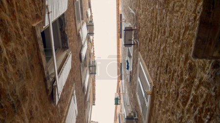 Photo for Narrow street with ancient stone buildings with wooden window blinds and red tile roofs at European old town. - Royalty Free Image