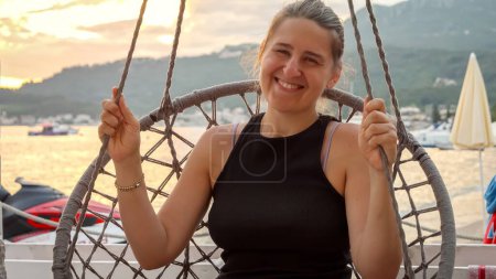 Foto de Retrato de mujer sonriente relajándose en la cuerda comer y balancearse contra la puesta del sol cielo sobre la playa de mar. - Imagen libre de derechos