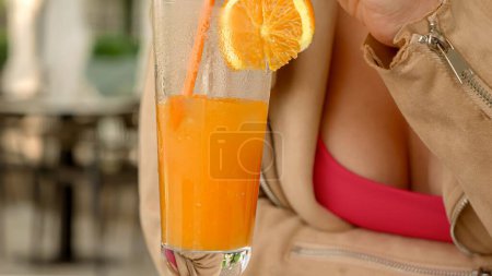 Téléchargez les photos : Gros plan de la femme agitant de la glace dans un verre de jus d'orange frais assis au restaurant. - en image libre de droit