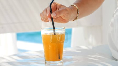 Téléchargez les photos : Dans un café de plage, une femme agite son jus d'orange avec une paille, capturant l'essence de l'été, la détente et la joie de vivre au bord de la mer. - en image libre de droit