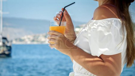 Téléchargez les photos : Gros plan de femme brune élégante profitant de son cocktail tout en se relaxant à la plage et en regardant les yachts et l'eau de mer. - en image libre de droit