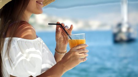 Photo for Closeup of beautiful woman drinking cocktail or juice with straw while enjoying summer vacation on the sea beach - Royalty Free Image