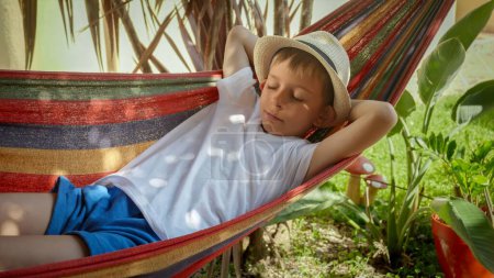 Photo for A boy sways and rests in a hammock at garden, portraying the sensations of summertime, treasured childhood memories, and the relaxation of a vacation. - Royalty Free Image