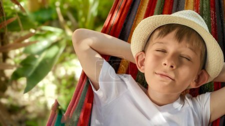 Foto de Un niño alegre, con una sonrisa soleada, columpios y salones en una hamaca de jardín, que encarna el espíritu del verano, la infancia sin preocupaciones y la esencia de unas vacaciones relajantes. - Imagen libre de derechos