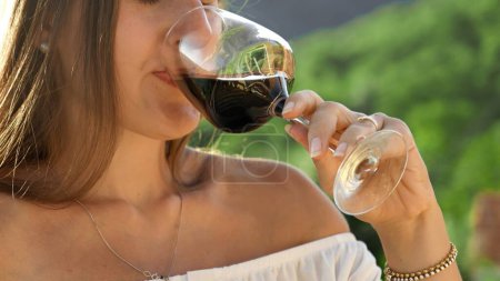 Photo for Closeup shot of elegant woman drinking red wine from glass against forest and mountain view. - Royalty Free Image