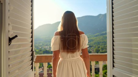 Photo for Young woman opening her window blinds and enjoying the mountain sunrise or sunset. Vacation and nature's beauty - Royalty Free Image
