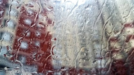 Téléchargez les photos : Gros plan de gouttelettes d'eau de pluie tombant sur le pare-brise de la voiture contre un immeuble vivant élevé en ville. - en image libre de droit