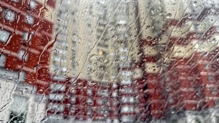 Téléchargez les photos : Des gouttelettes d'eau de pluie tombent et coulent sur le pare-brise de la voiture en ville. - en image libre de droit