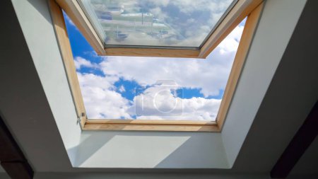 Foto de Mirando las nubes que pasan volando por el cielo azul a través de la ventana abierta del ático en el techo de la casa. - Imagen libre de derechos