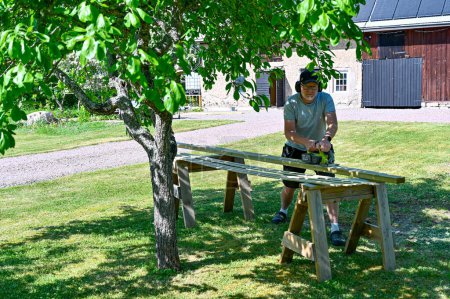 Téléchargez les photos : Homme debout dans le jardin planches à découper avec scie circulaire Kumla Suède juin 6 2023 - en image libre de droit