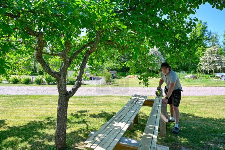 Téléchargez les photos : Homme debout dans le jardin planches à découper avec scie circulaire Kumla Suède juin 6 2023 - en image libre de droit