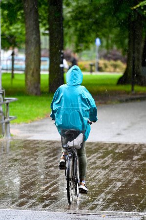 Photo for Woman riding bike over bridge a rainy day in a turquoise rain jacket Orebro Sweden august 9 2023 - Royalty Free Image