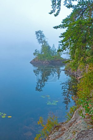 Téléchargez les photos : Eaux calmes avec une île calme dans le brouillard du matin sur le lac Jenny dans la zone de canot d'eau limitrophe dans le Minnesota - en image libre de droit