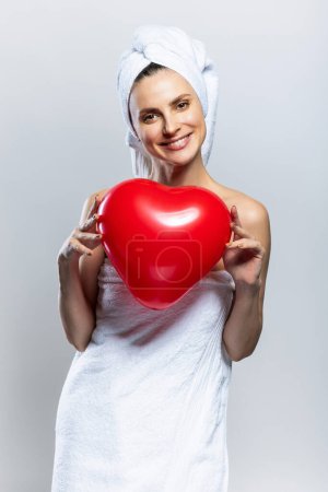 Foto de Mujer hermosa y alegre con toallas blancas y sosteniendo un corazón rojo. Día de San Valentín - Imagen libre de derechos