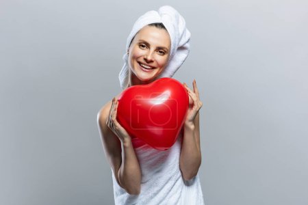 Foto de Mujer hermosa y alegre con toallas blancas y sosteniendo un corazón rojo. Día de San Valentín - Imagen libre de derechos