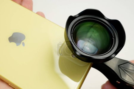 Foto de Dnipro Ukraine - 04 04 22: yellow smartphone iPhone with external Apexel lens on clip on white. An additional portrait lens and clip are supplied with the mobile phone, closeup - Imagen libre de derechos