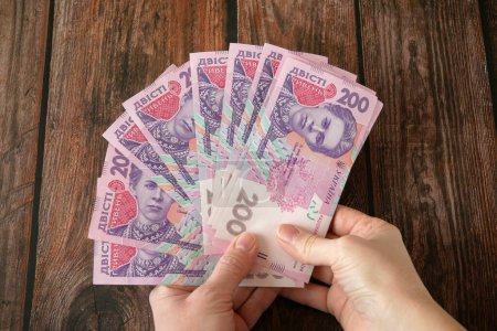 Photo for Hand holding big stack of Ukrainian hryvnia on wooden background. money cash, closeup - Royalty Free Image