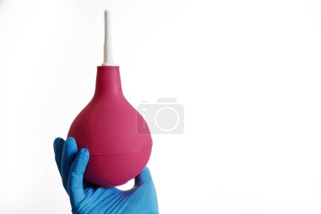 Téléchargez les photos : Médecin en gants médicaux bleus tenant un lavement rouge isolé sur fond blanc, concept, gros plan - en image libre de droit