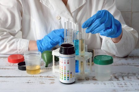 Photo for Medical laboratory assistant taking test tube with liquids, test with urine, Scientist doctor looking at sample in test tube. Laboratory analysis. Closeup - Royalty Free Image