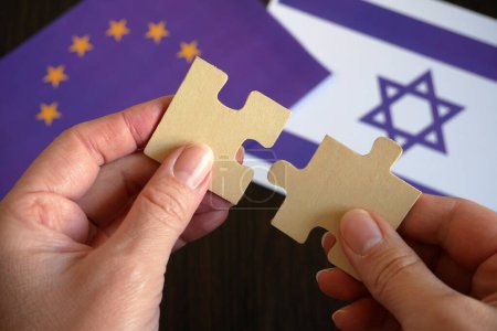 Téléchargez les photos : Mains tiennent deux pièces d'un puzzle sur le fond des drapeaux Israël et l'Union européenne, signe et simbol, concept, gros plan - en image libre de droit