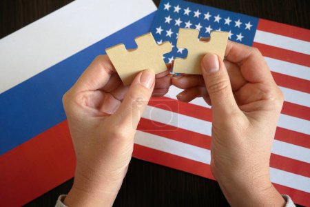 Téléchargez les photos : Mains tiennent deux pièces d'un puzzle sur le fond des drapeaux USA et Russie, signe et simbol, concept, gros plan - en image libre de droit