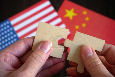 Téléchargez les photos : Mains tenir deux pièces d'un puzzle sur le fond des drapeaux États-Unis et la Chine, amitié et partenariat de deux pays concept, gros plan - en image libre de droit