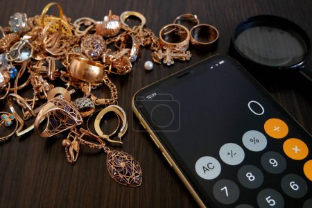 Foto de Concepto de tienda de empeño, calculadora, una gran cantidad de joyas de oro y una lupa en una mesa de madera oscura, vista superior, puesta plana - Imagen libre de derechos