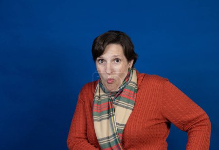 Photo for Woman in an orange sweater in the studio. High-quality photo was taken on a blue background with a campy pose. - Royalty Free Image
