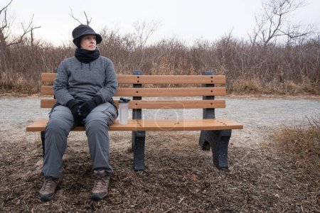Photo for Sad woman sitting on a bench in winter in a coastal new England setting - Royalty Free Image