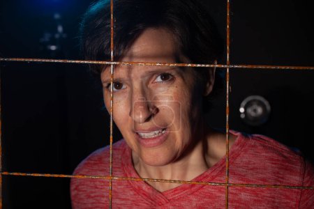 Téléchargez les photos : Image Low Key d'une femme derrière un fil métallique rouillé avec rétro-éclairage. Image conceptuelle féminine piégée ou frustrée - en image libre de droit