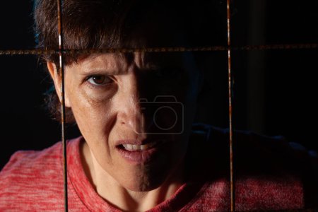 Téléchargez les photos : Low Key image of a woman behind rusty metal wire with backlighting. Trapped or frustrated female concept image - en image libre de droit