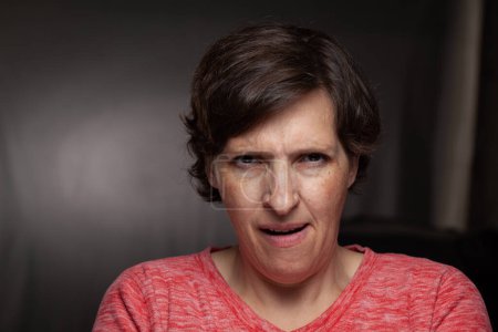 Téléchargez les photos : Low-key image of an older woman looking annoyed. Photo with studio lights visible behind her - en image libre de droit
