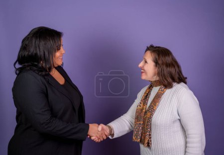 A tall Hispanic businesswoman meets an older caucasian woman with a handshake diversity in the workplace concept.