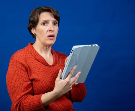 Téléchargez les photos : Femme inquiète travaillant sur une tablette dans le studio sur un fond bleu - en image libre de droit