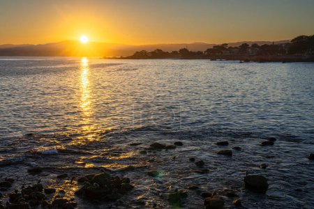 Téléchargez les photos : Le soleil se couche sur l'océan, projetant une lueur chaude sur l'eau. Le ciel est un mélange de teintes orange et rose, créant une atmosphère sereine et paisible - en image libre de droit