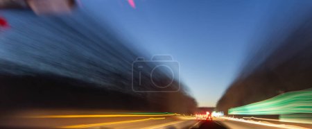 Téléchargez les photos : Un plan flou d'une autoroute la nuit avec une voiture au premier plan. La scène est sombre et lunatique, avec les phares de la voiture illuminant la route - en image libre de droit
