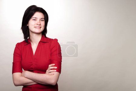 Téléchargez les photos : Une femme en chemise rouge sourit et croise les bras. Elle a l'air confiante et heureuse. Concept de positivité et d'auto-assurance - en image libre de droit