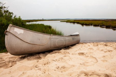 Téléchargez les photos : Un canot est assis sur la plage à côté d'un plan d'eau par une journée nuageuse - en image libre de droit