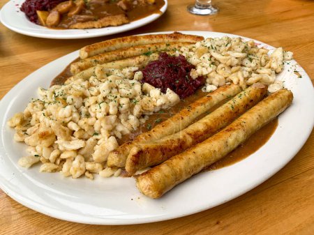 Téléchargez les photos : Une assiette de nourriture allemande avec des saucisses de poulet bratwurst, pommes de terre et chou rouge sur assiette blanche à la lumière naturelle - en image libre de droit