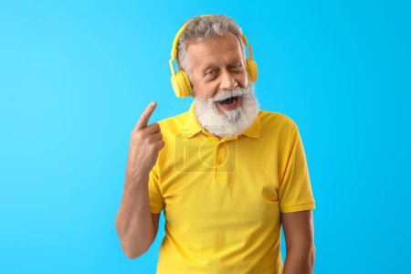 Senior bearded man pointing at headphones on blue background