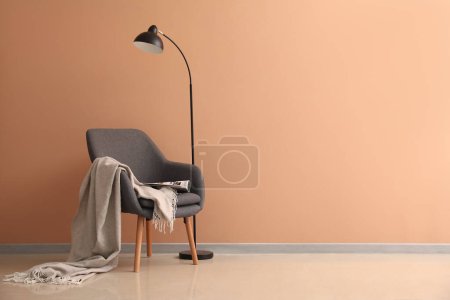 Foto de Sillón suave con cuadros, cargador y lámpara cerca de la pared beige - Imagen libre de derechos