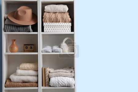Photo for Shelving unit with sweaters, hat and decor near blue wall - Royalty Free Image