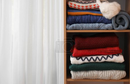 Shelving unit with folded sweaters near light curtain, closeup