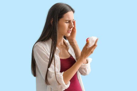 Young pregnant woman with nosebleed and tissue on blue background
