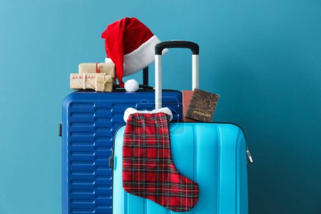 Téléchargez les photos : Valises avec chapeau de Père Noël, passeports et cadeaux de Noël près du mur bleu - en image libre de droit