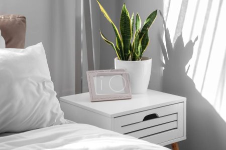 Nachttisch mit Fotorahmen und Zimmerpflanze im hellen Schlafzimmer
