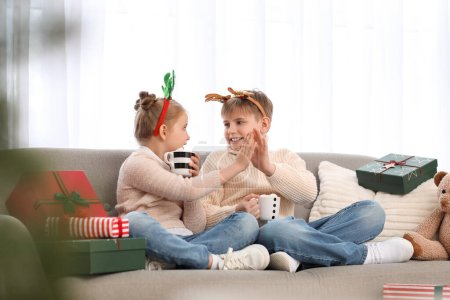 Foto de Niños pequeños con tazas de cacao dándose los cinco en casa en la víspera de Navidad - Imagen libre de derechos
